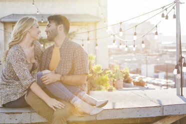 Happy couple sitting on rooftop, embracing each other - WESTF22829