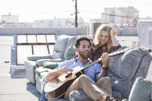 Paar auf der Dachterrasse sitzt auf dem Sofa und spielt Gitarre - WESTF22840