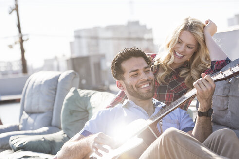 Paar auf der Dachterrasse sitzt auf dem Sofa und spielt Gitarre - WESTF22841