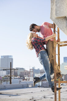 Junges Paar küsst sich auf einer Feuerleiter auf einem Dach - WESTF22863