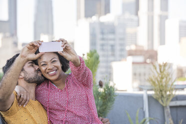 Ein Paar sitzt auf einer Dachterrasse und macht Selfies mit dem Smartphone - WESTF22868