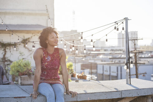 Junge Frau sitzt auf einer Dachterrasse und genießt die Sonne - WESTF22875