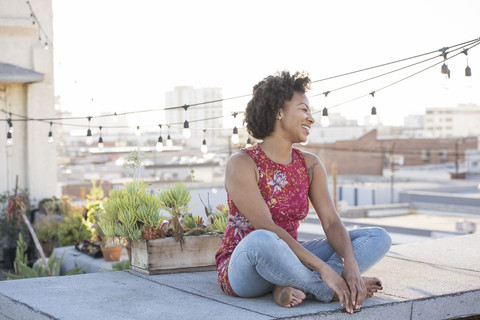 Junge Frau sitzt auf einer Dachterrasse und genießt die Sonne, lizenzfreies Stockfoto