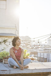 Young woman sitting on rooftop terrace, enjoying the sun - WESTF22878