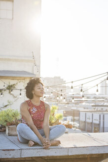 Junge Frau sitzt auf einer Dachterrasse und genießt die Sonne - WESTF22878