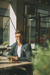 Smiling man sitting in a coffee shop with glass of tea - CHAF01819