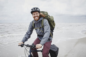 Germany, Schleswig-Holstein, St Peter-Ording, happy young man riding bicycle on the beach - RORF00715