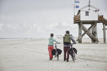 Germany, Schleswig-Holstein, St Peter-Ording, couple pushing bicycles on the beach - RORF00716