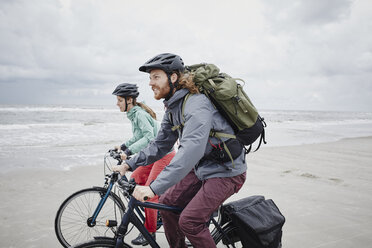 Germany, Schleswig-Holstein, St Peter-Ording, couple riding bicycle on the beach - RORF00719