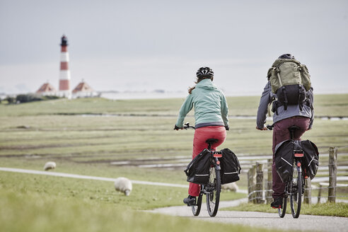 Deutschland, Schleswig-Holstein, Eiderstedt, Paar fährt Fahrrad in der Nähe des Leuchtturms Westerheversand - RORF00720