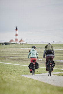 Deutschland, Schleswig-Holstein, Eiderstedt, Paar fährt Fahrrad in der Nähe des Leuchtturms Westerheversand - RORF00721