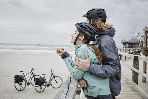 Germany, Schleswig-Holstein, St Peter-Ording, couple on a bicycle trip having a break on jetty at the beach stock photo