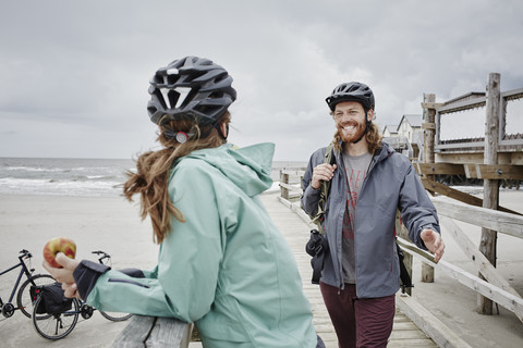 Deutschland, Schleswig-Holstein, St. Peter-Ording, Pärchen auf Fahrradtour mit Pause auf Steg am Strand, lizenzfreies Stockfoto