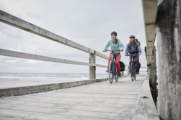 Germany, Schleswig-Holstein, St Peter-Ording, couple riding bicycle on jetty at the beach - RORF00726