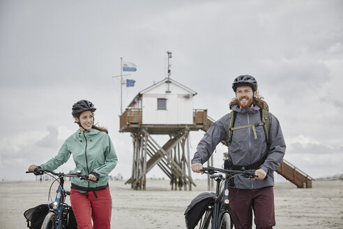 Deutschland, Schleswig-Holstein, St. Peter-Ording, Paar schiebt Fahrräder am Strand - RORF00728