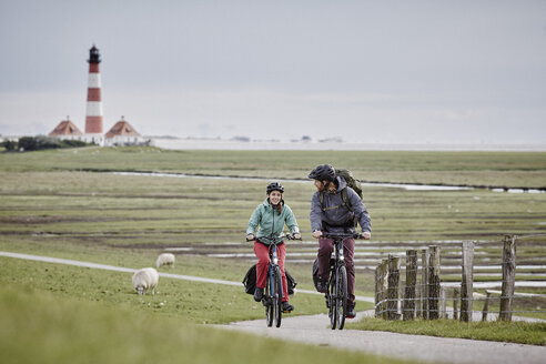 Deutschland, Schleswig-Holstein, Eiderstedt, Paar fährt Fahrrad in der Nähe des Leuchtturms Westerheversand - RORF00741