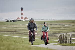 Germany, Schleswig-Holstein, Eiderstedt, couple riding bicycle near Westerheversand Lighthouse - RORF00743