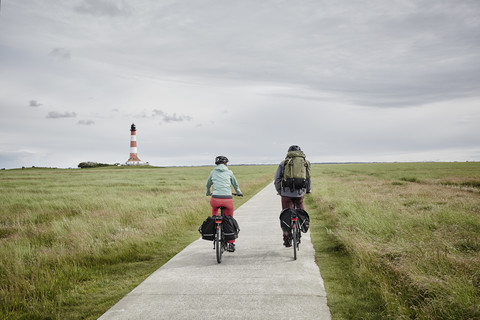 Germany, Schleswig-Holstein, Eiderstedt, couple riding bicycle near Westerheversand Lighthouse stock photo