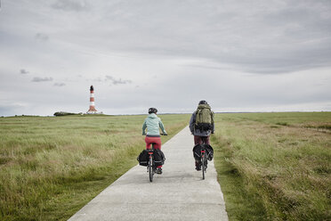 Deutschland, Schleswig-Holstein, Eiderstedt, Paar fährt Fahrrad in der Nähe des Leuchtturms Westerheversand - RORF00744