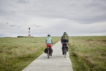 Germany, Schleswig-Holstein, Eiderstedt, couple riding bicycle near Westerheversand Lighthouse - RORF00744