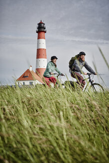 Deutschland, Schleswig-Holstein, Eiderstedt, Paar fährt Fahrrad in der Nähe des Leuchtturms Westerheversand - RORF00745