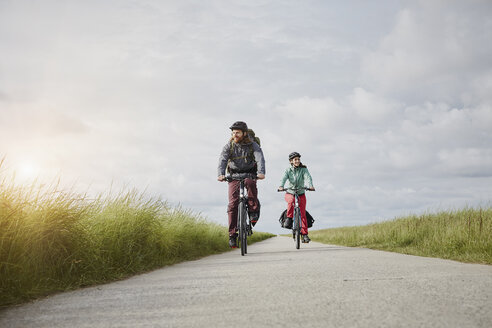 Deutschland, Schleswig-Holstein, Eiderstedt, Paar fährt mit dem Fahrrad auf einem Weg durch Salzwiesen - RORF00749