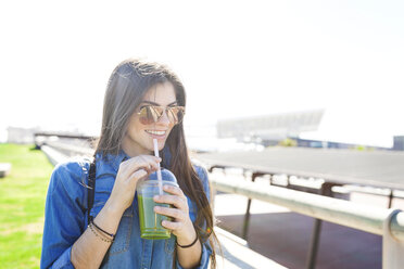 Spain, Barcelona, portrait of smiling young woman with green beverage - VABF01270