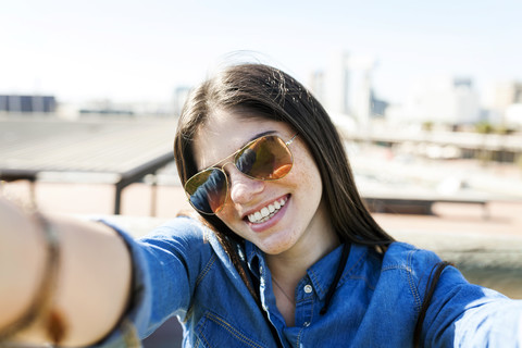 Portrait of smiling young woman wearing sunglasses taking selfie stock photo