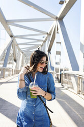 Spain, Barcelona, laughing young woman with beverage on a bridge - VABF01274