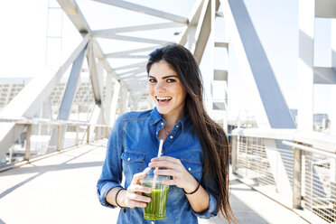Spanien, Barcelona, Porträt einer lächelnden jungen Frau mit Getränk auf einer Brücke - VABF01276