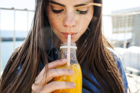 Junge Frau mit Sommersprossen trinkt Orangensaft, lizenzfreies Stockfoto
