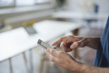 Nahaufnahme eines Mannes, der im Büro ein Mobiltelefon benutzt - KNSF01196