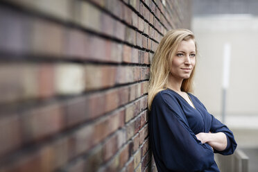 Portrait of smiling blond young woman leaning against brick wall - DMOF00004