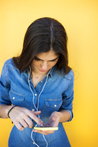 Junge Frau mit Kopfhörern und Smartphone vor einer bunten Wand, lizenzfreies Stockfoto