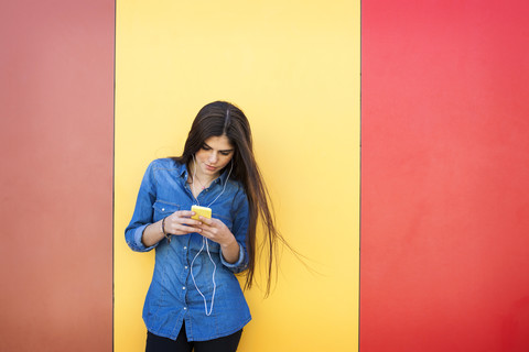 Young woman with earphones and smartphone standing in front of colourful wall stock photo