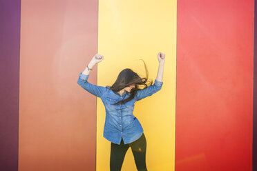 Happy young woman dancing in front of colourful wall - VABF01290