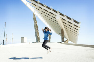 Young woman jumping in the air with solar panels in background - VABF01293