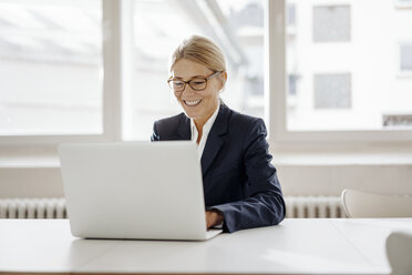 Lächelnde Geschäftsfrau mit Laptop im Büro - JOSF00701
