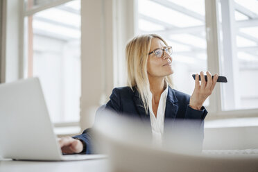 Businesswoman using laptop and cell phone in office - JOSF00706