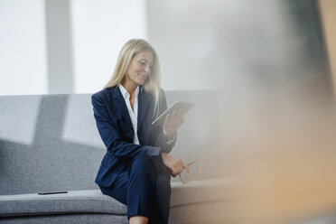 Lächelnde Geschäftsfrau, die auf einer Couch sitzt und ein Tablet hält - JOSF00708