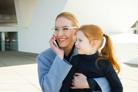 Lächelnde Geschäftsfrau am Telefon, die ihre Tochter umarmt, lizenzfreies Stockfoto