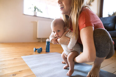 Smiling mother with baby and dumbbells at home - HAPF01367