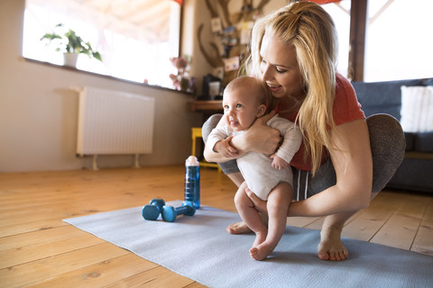 Smiling mother with baby and dumbbells at home stock photo