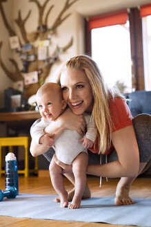 Lächelnde Mutter mit Baby und Fitnessgeräten zu Hause - HAPF01370