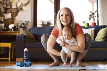 Smiling mother with baby and dumbbells at home - HAPF01371