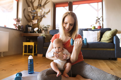 Smiling mother with baby exercising with dumbbell at home stock photo