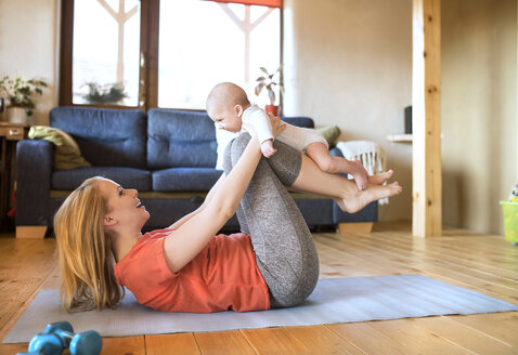 Glückliche Mutter hebt ihr Baby zu Hause auf einer Matte liegend hoch - HAPF01380