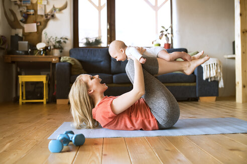 Glückliche Mutter hebt ihr Baby zu Hause auf einer Matte liegend hoch - HAPF01381