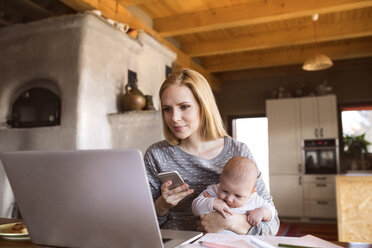 Mother with baby at home using laptop and cell phone - HAPF01383
