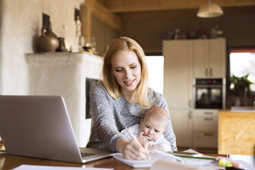 Mutter mit Baby zu Hause, die einen Laptop benutzt und sich Notizen macht - HAPF01385